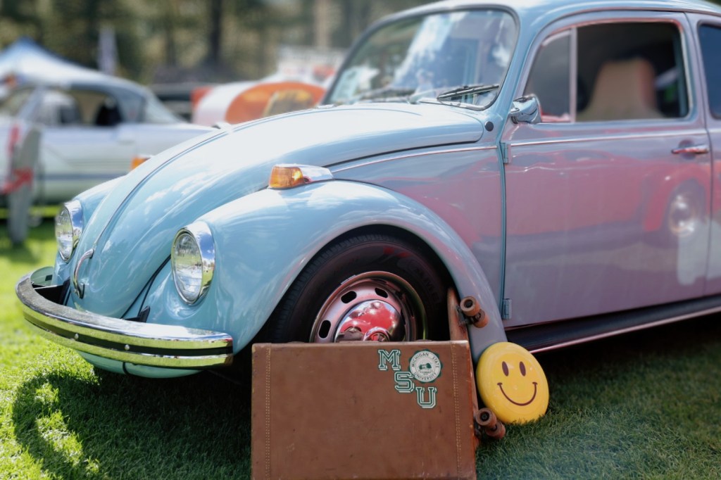 An antique Volkswagen Beetle posed with a vintage suitcase and skateboard