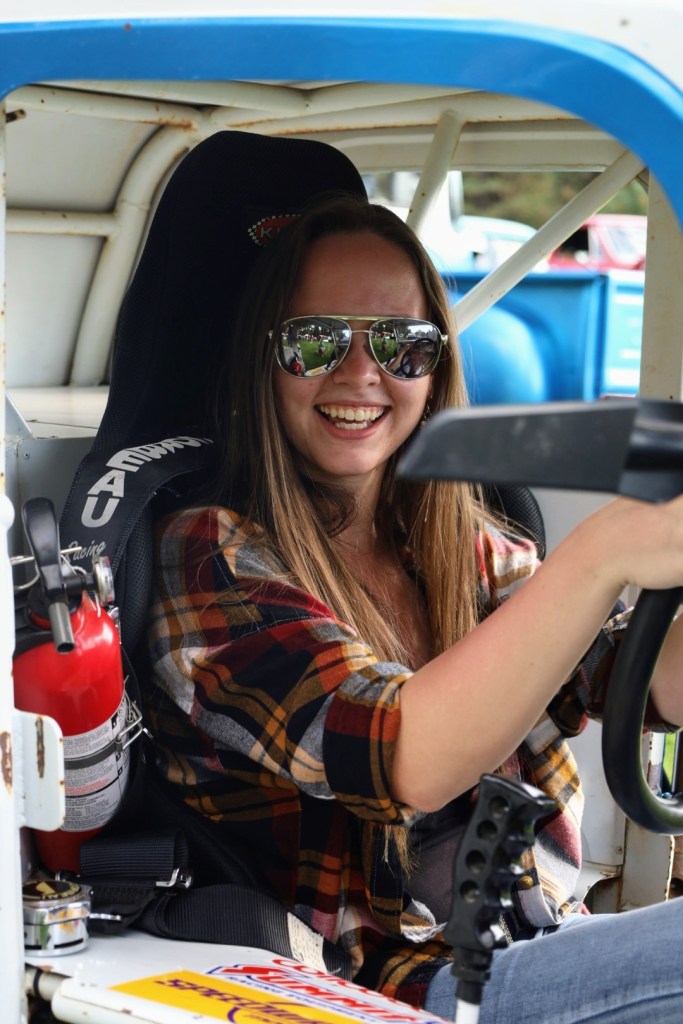 A model smile delightedly while posing in a functioning midget race car