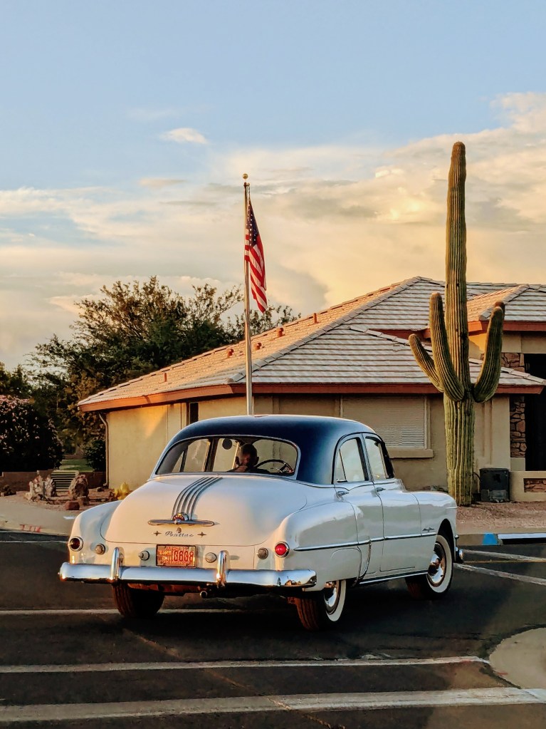 An antique Pontiac driving in an Arizona neighborhood