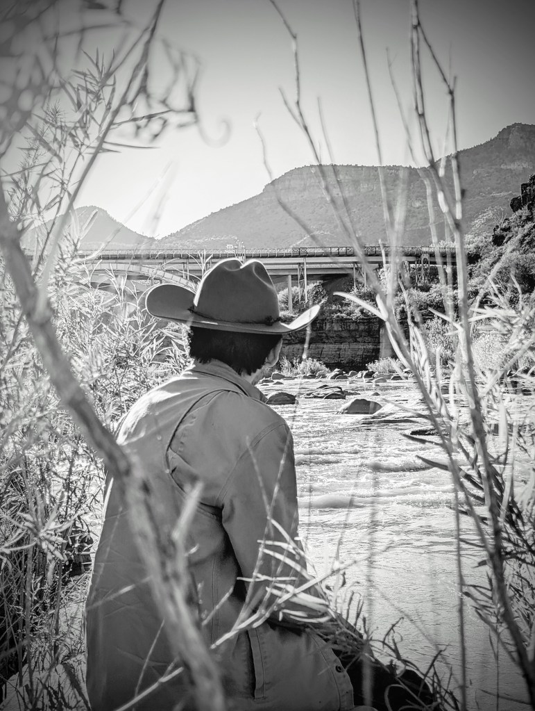 A man wearing a cowboy hat staring at a river