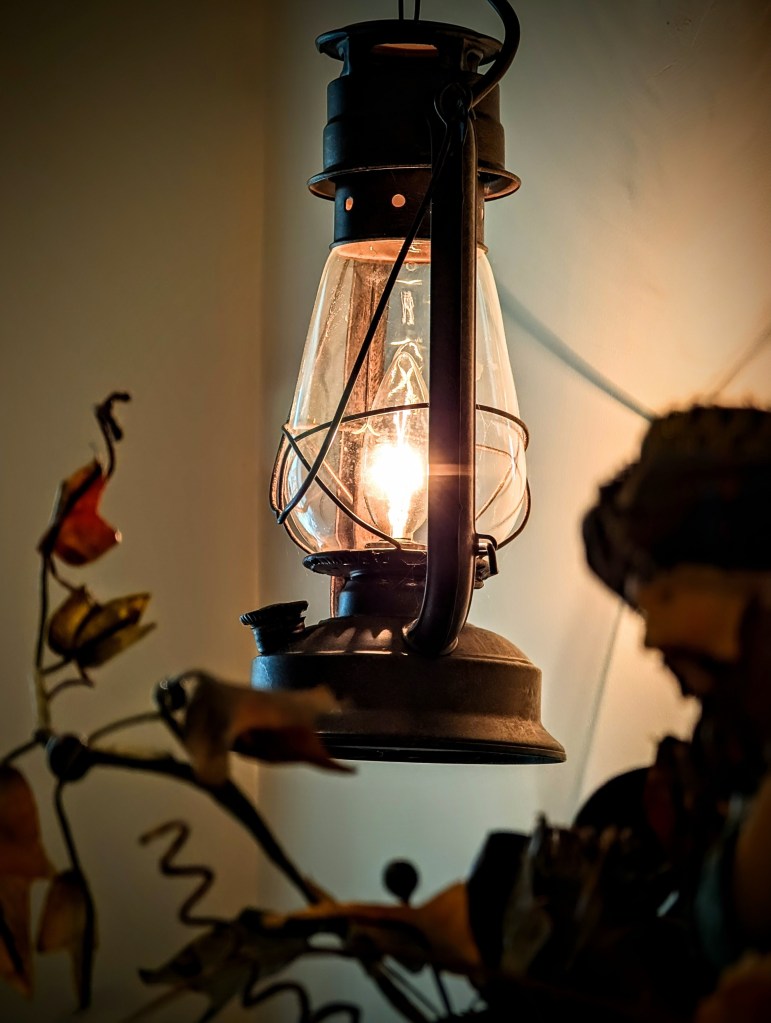 A rustic lamp hangs on the wall, framed by blurred foreground elements